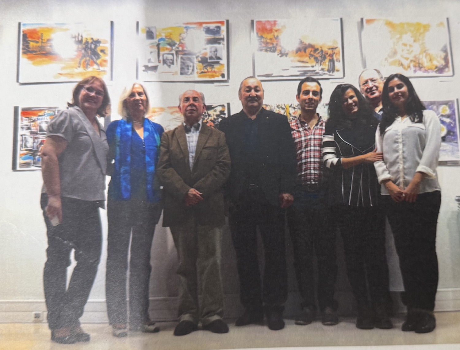 Rouslam Botiev com convidados numa exposição, diante de uma parede com as suas aguarelas