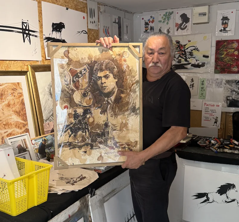 Rouslam Botiev holding a finished original painting titled Alfama, framed in light oak, in his Alfama atelier in Lisbon