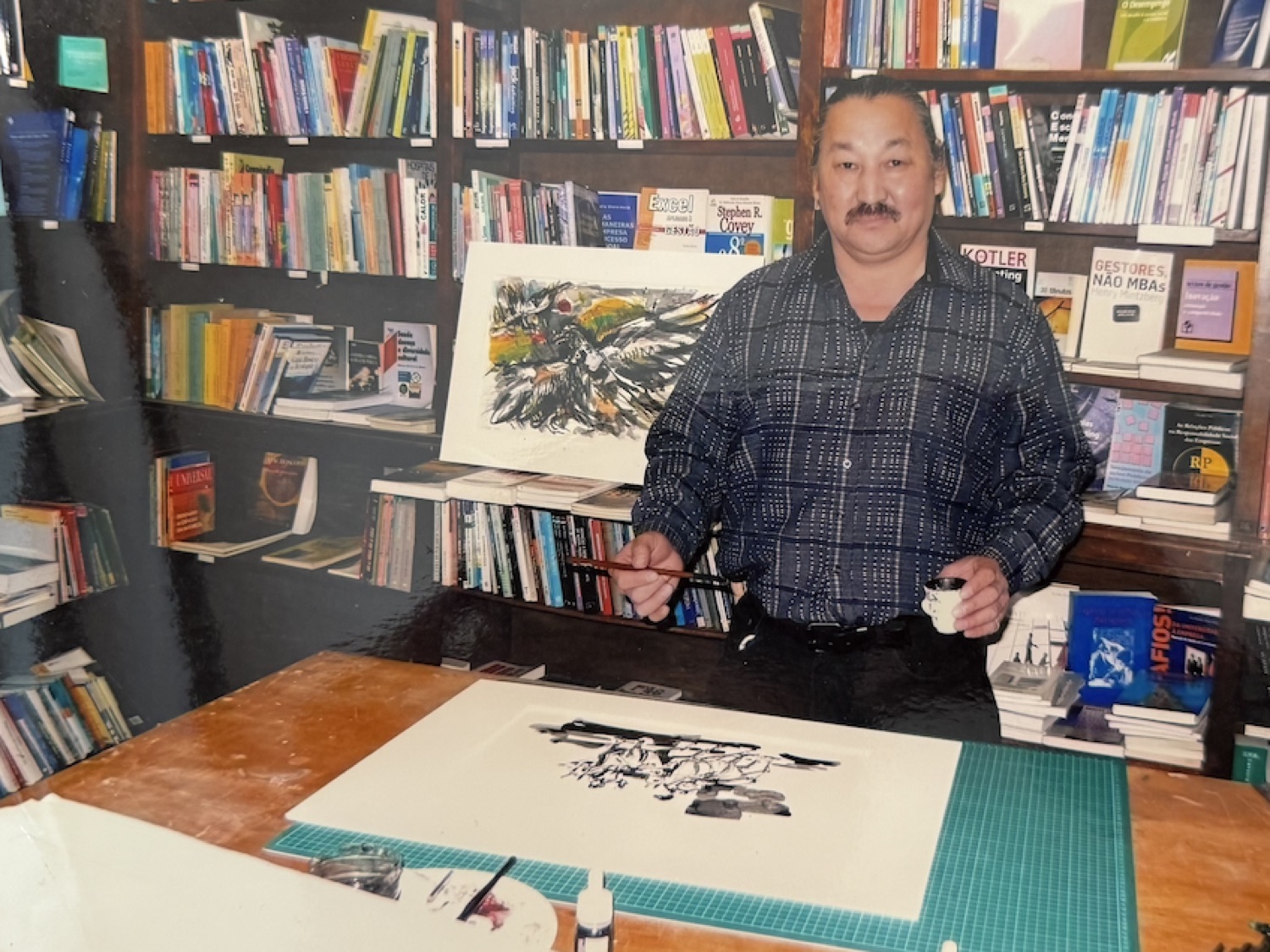 Rouslam Botiev a pintar a tinta-da-china, pincel e chávena de café na mão, entre as estantes de uma livraria de Lisboa